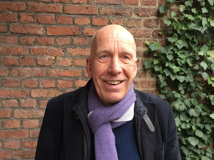 freundlicher Herr ohne Haare mit Sakko ein einem Schal, welcher die Farbe Lila hat